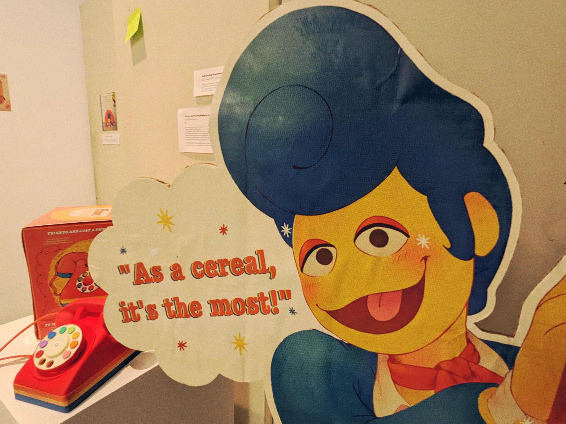 A photograph of a Wally Darling Crispy Sweets advertisement cardboard standee, it's a closeup on Wally's face, and behind him you can see a toy telephone on display
