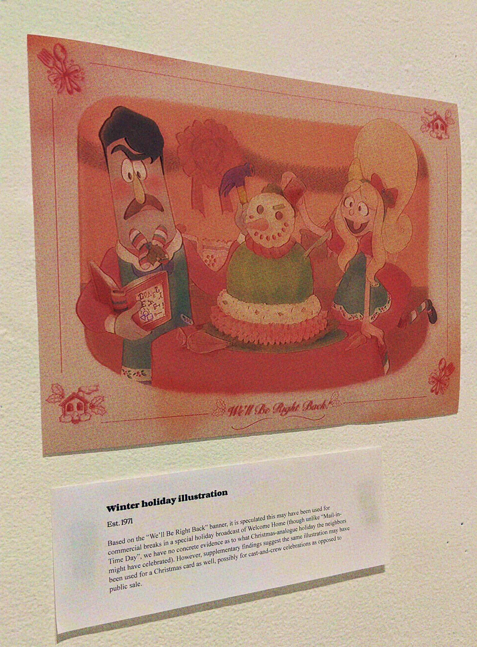 A photo of a wall with an illustration and exhibit card. The card reads: 'Winter holiday illustration, Est. 1971. Based on the 'We'll Be Right Back' banner, it is speculated this may have been used for commercial breaks in a special holiday broadcast of Welcome Home (though unlike 'Mail-in-Time Day', we have no concrete evidence as to what Christmas-analogue holiday the neighbors might have celebrated). However, supplementary findings suggest the same illustration may have been used for a Christmas card as well, possibly for cast-and-crew celebrations as opposed to public sale.' The illustration shows Julie and Frank, Frank is looking at a caroling book curiously, while Julie decorates a snowman looking gelatin dish, smiling wide. Text under it reads 'We'll Be Right Back!'