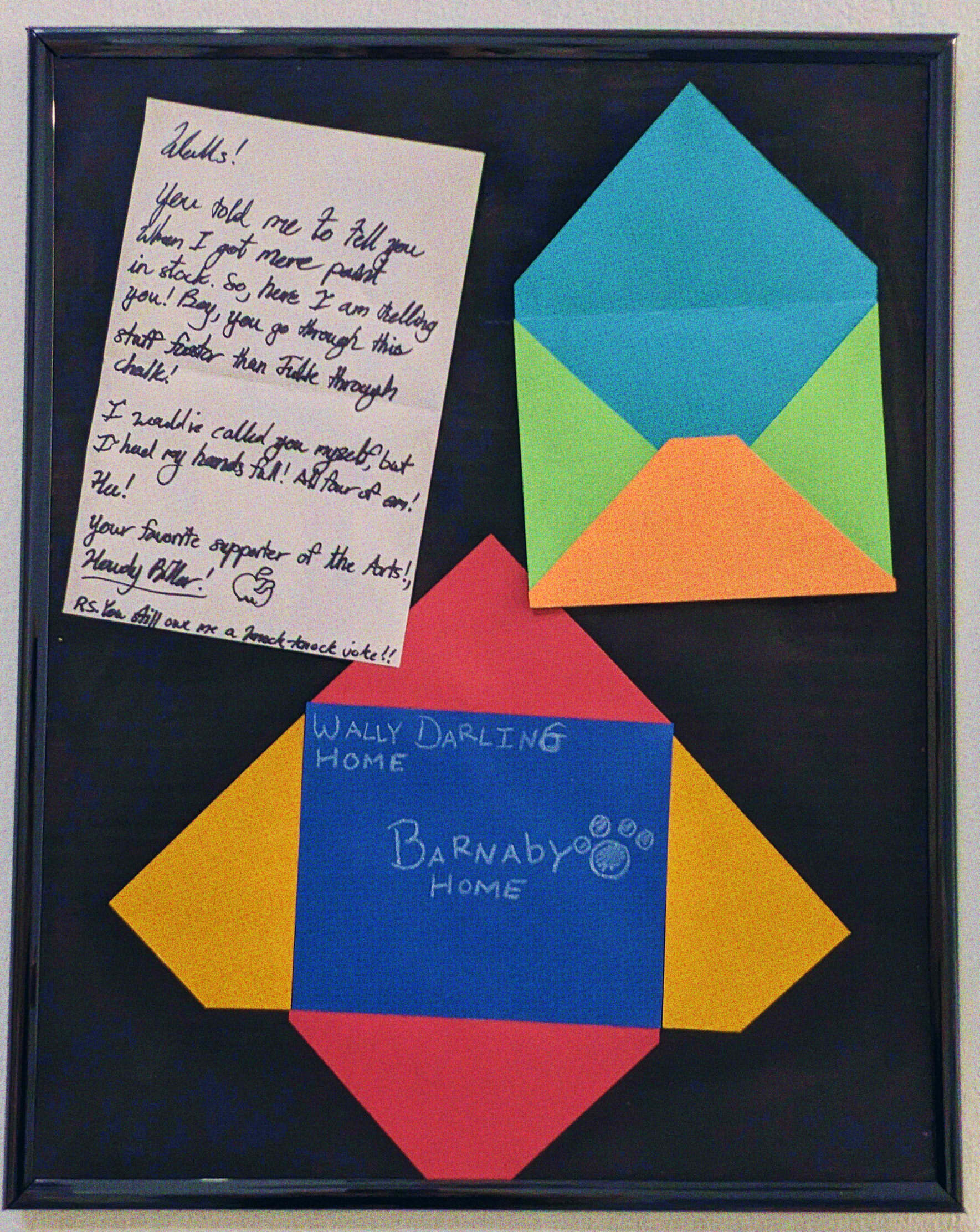 A framed display of two brightly colored envelopes, one from Wally to Barnaby. Alongside one open letter reading: 'Walls! You told me to tell you when I got more paint in stock. So, here I am telling you! Boy, you go through this stuff faster than Julie through chalk! I would've called you myself, byt I had my hands full! All for of em! Hee! You favorite supporter of the Arts!, Howdy Pillar! P.S. You still owe me a knock-knock joke!!'