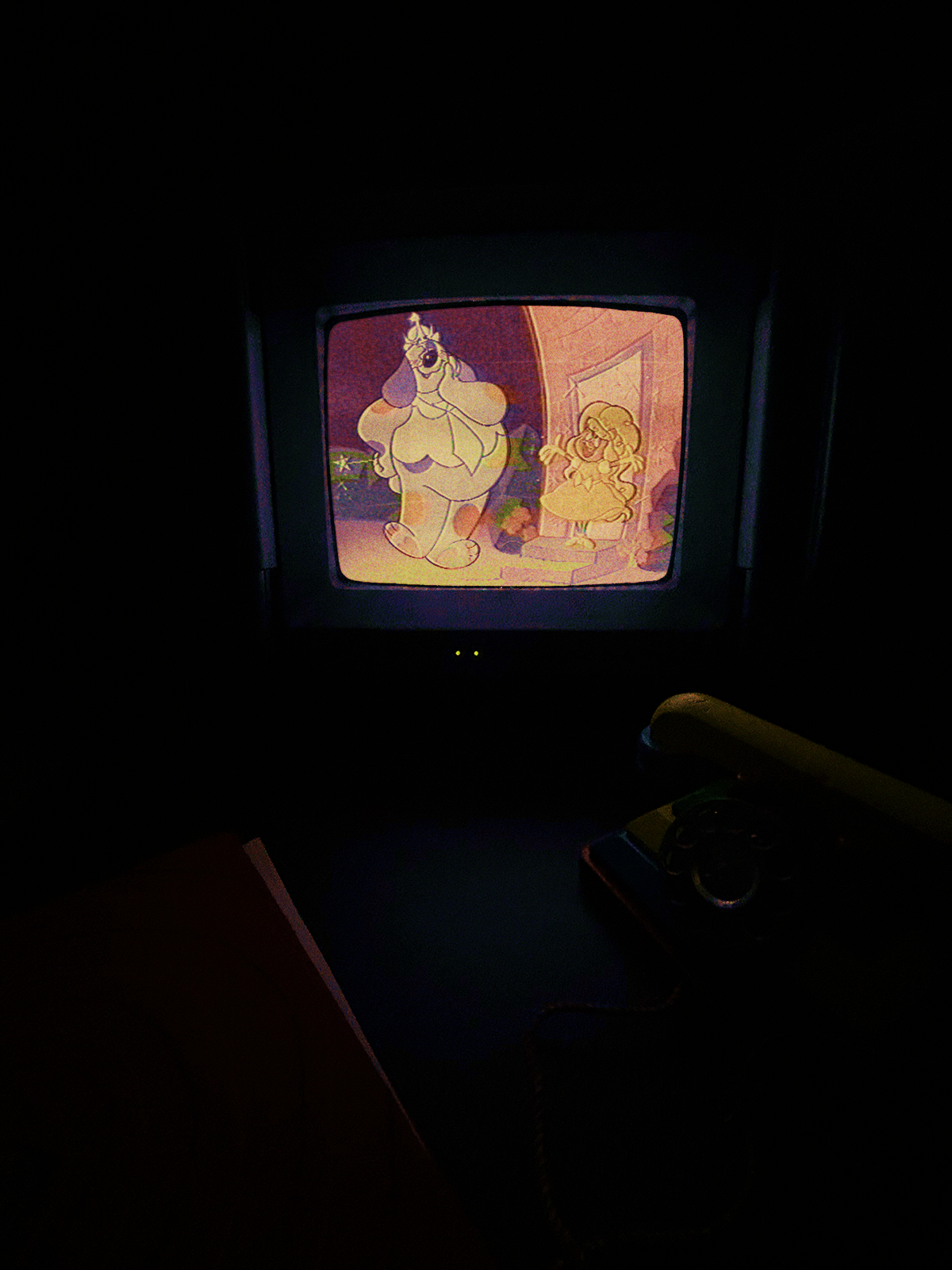 A photograph of Julie-rella playing on a CRT in a dark room. The still we see is Julie on the same doorstep, now wearing a dress and smiling, while Barnaby looks pleased.